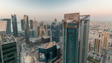 Batı Körfezi bölgesinin ufuk çizgisi Doha 'da gece gündüz geçiş zamanı, Katar. Aydınlatılmış modern gökdelenler. Sabah güneş doğmadan önce çatıdan gökyüzü manzarası.