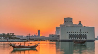 Katar 'ın Doha kentindeki İslam Sanatları Müzesi yakınlarındaki günbatımında, arkasında yükselen gökdelenler görülüyor. Öndeki eski tekneler.