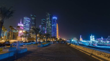 Geceleri Doha 'nın ufuk çizgisi Corniche Timelapse hiperlapse, Katar' dan görülebiliyor. Palmiyeler ve botlar yana. Aydınlatılmış gökdelenler ve kuleler