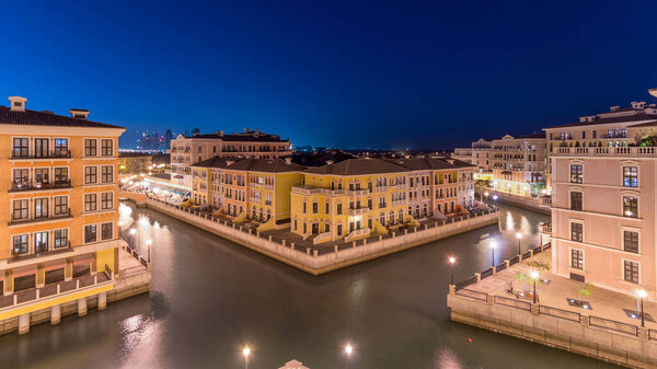 Вид сверху с высоты канала в Венецианском квартале Qanat Quartier Жемчужного участка Дохи день и ночь, переходный период, Катар. Вечернее освещение отражается в воде