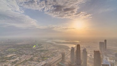 Dubai timelapse Downtown ve Business bay üzerinde Gündoğumu. Bulutlu turuncu gökyüzü ve puslu hava. Burç Halife bakış açısından kuleler ve gökdelenler ile havadan görünüm.