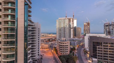 Dubai Marina 'da aydınlık gökdelenler ve gece gündüz gezinti güvertesi geçiş zamanı. Yol trafiği olan modern kuleler ve tekneler. Birleşik Arap Emirlikleri