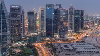 Jumeirah Lake Towers yerleşim bölgesi Dubai Marina yakınında gece geçiş timelapse gün havadan. Işıklı modern gökdelenler ve yukarıdan park