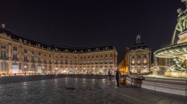 Panorama, Place de la Bourse 'u ve Fransa' nın Bordeaux şehrindeki çeşmeleri gösteriyor. Aydınlatılmış tarihi binalar büyük meydanın sınırında. Trafik ve sokakta hareket sahneyi güçlendirir