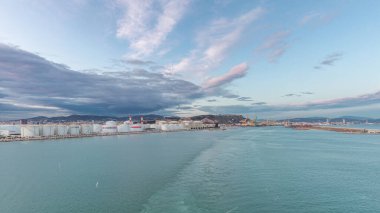 Gün batımında açık denizde yelken açan gemiden dalgalı ve limanlı deniz manzarası. Barselona kıyısı, İspanya
