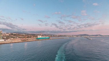 Gün batımında açık denizde yelken açan gemiden dalgalı ve limanlı deniz manzarası. Marsilya kıyısı, Fransa