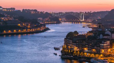 Day to night transition aerial view of the historic city of Porto, Portugal panoramic timelapse from the Dom Luiz bridge. Illuminated waterfront and curved river from above