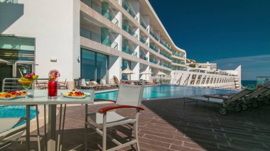 Güneşli yansımaları ve mavi suyu olan küçük bir otel yüzme havuzu ve meyveli bir masa.