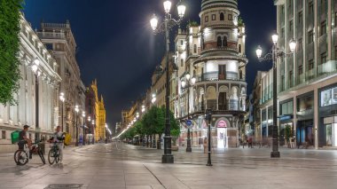 Avenida de la Constitucion, Seville, İspanya 'da günden geceye zaman dilimi. Iconic Adriatica binası gün batımından sonra parlıyor. Modern sokak lambaları, yayalar ve şehir atmosferine sahip tarihi mimari
