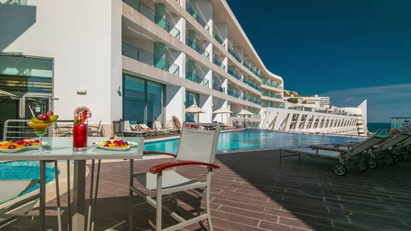 Güneşli yansımaları ve mavi suyu olan küçük bir otel yüzme havuzu ve meyveli bir masa.