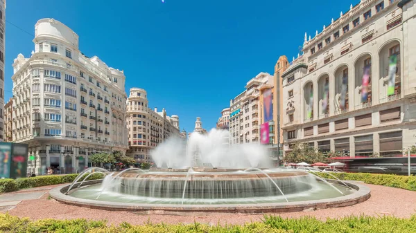 Panorama, İspanya 'nın Valencia şehrinde Belediye Meydanı' nda (Plaza del Ayuntamiento Meydanı) fıskiyeyi gösteriyor. Büyük mimari, çiçek açan yeşillik ve mavi gökyüzünün altında su jetleri. İnsanlar meydanda geziniyor.