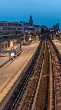 Almanya 'nın Hamburg kentindeki Landungsbrucken istasyonuna ulaşan trenlerin hava gününden geceye geçiş zamanı. Metroya binen insanlar, Elbphilharmonie, liman ve marina ile panoramik manzara