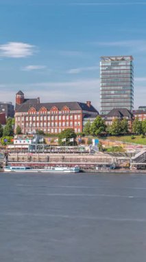 Hamburg limanına giriş ve çıkış yapan bir feribotun zaman çizelgesi. İskelede yolcuları var ve merdivenlerde ilerliyor. Arkaplanda Elbe nehri boyunca tarihi ve modern binalar var. Almanya