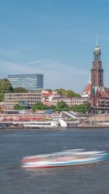 Elbe nehir kenarı ve Hamburg, Almanya 'daki St. Michaels kilise kulesinin panoramik zaman çizelgesi. İskeleye yakın teknelerle manzara, Jan Fedder gezinti güvertesi ve oradan geçen feribotlar. Nehir kenarındaki canlı şehir manzarası