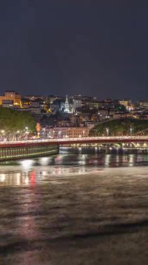 Saone Nehri üzerindeki kırmızı asma köprü ile Lyons şehir manzarasının gece zaman çizelgesi, aydınlatılmış kıyı şeridi gece boyunca suya yansıdı. Fransa