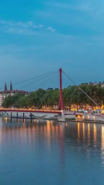 Lyon 'daki Saone Nehri' nin üzerindeki Palais du Justice Köprüsü 'nde, günden geceye geçiş. Rıhtımdaki aydınlık binalar gün batımından sonra suya yansıyor.