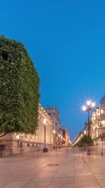 Avenida de la Constitucion, Seville, İspanya 'da günden geceye zaman dilimi. Modern sokak lambaları, yayalar ve kentsel atmosferi olan tarihi mimari. Iconic Adriatica binası gün batımından sonra parlıyor.