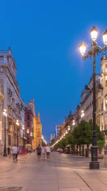 Avenida de la Constitucion, Seville, İspanya 'da günden geceye zaman dilimi. Iconic Adriatica binası gün batımından sonra parlıyor. Modern sokak lambaları, yayalar ve şehir atmosferine sahip tarihi mimari