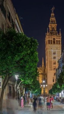 Barrio Santa Cruz 'un Seville, İspanya' daki gece zamanı. Arka planda Giralda kulesi aydınlanıyor. Turistler ve yerliler kafeler ve dükkanlarla dolu büyüleyici kaldırım taşları caddelerinde yürüyorlar..