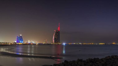 Dubai silueti, Burj Al-Arap oteli ile gündüz gece geçiş zamanı. Uçurtma kumsalının manzarası. Dubai marina kuleleri arka planda. Jumeirah plajının önünde yapay bir adaya inşa edilmiş bir otel..