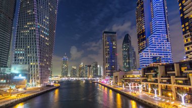 Dubai Marina rıhtımı. Köprüden gece, gündüz kuleleri ve yatları var. Geçiş zamanı, Birleşik Arap Emirlikleri. Gün batımından sonra gökdelenler ve kanallar