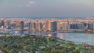 Güneş batarken Dubai Deresi ve Deira 'da arka planda deniz bulunan Park ve Mavi Nehir yakınlarındaki yeni modern binaların akşam manzarası Birleşik Arap Emirlikleri