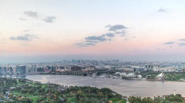 Parkta yeşil ağaçları olan yeni modern şehrin silueti Dubai Creek, Dubai 'deki Aerial Timelapse, Birleşik Arap Emirlikleri' nde gün batımında