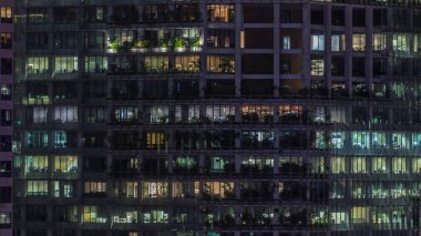 Gece vakti büyük pencereleri olan modern ofis binası. Yakın görüş, parlayan pencereler ve Singapur 'da yaşayan bazı insanlar.