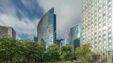 Panorama modern ofis binalarının zaman çizelgesini gösteriyor. Parktaki yeşil ağaçlar tarafından çerçevelenmiş parlak mavi gökyüzü üzerinde yansımaları ve röfleleri olan cam gökdelenler. Brüksel 'de güneş ışığı ve geçen bulutlar