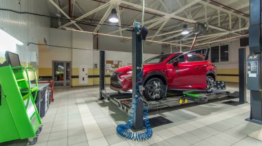Tekerlek hizalaması için tekerlekli sensörlü araç servis istasyonunun zaman ayarlı atölyesinde kontrol ediliyor. Araba asansörde hareket ediyor