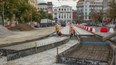 Beton, turuncu üniformalı ve mikser makineli birçok işçiyle yol inşaatı için özel plakaların yanında çalışıyor. Tramvay raylarının yeniden inşası