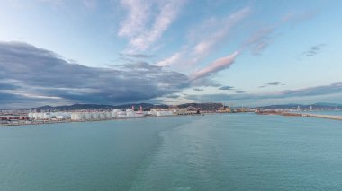 Gün batımında açık denizde yelken açan gemiden dalgalı ve limanlı deniz manzarası. Barselona kıyısı, İspanya