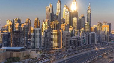 Dubai Yat Limanı günbatımı hava timelapse sırasında Birleşik Arap Emirlikleri kuleleri. Güneş gökdelenler uzun gölgeler ile yansıyan. Yolda trafik ile Jlt üzerinden üstten görünüm