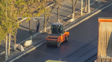 Yeni yol inşaatında çalışan yol silindirlerinin geniş bir manzarası var. Yeni cadde asfaltlanırken görüntüyü kapat