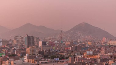 Gün batımında Lima şehrinin panoramik ufuk çizgisi ve birçok binanın havadan zaman çizelgesi. Arka planda tepeler olan fakir evler. Sokakta trafik vardı. Lima, Peru