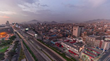 Via Expresa otoyolu ve Peru Ulusal Stadyumu yakınlarındaki gün batımı saatinde trafiği olan metropolitan otobüsünün hava manzarası. Evler ve şehrin arka planında dağlar olan silueti. Lima, Peru