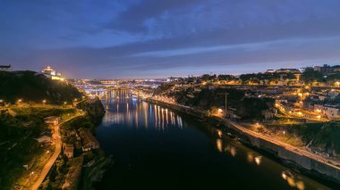 Day to night transition aerial view of the historic city of Porto, Portugal panoramic timelapse with the Dom Luiz bridge. Illuminated waterfront reflected in the river from above