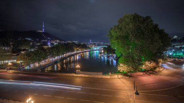 Gürcistan 'ın Tiflis şehrinde ahşap oyulmuş balkonlu renkli geleneksel evleri gösteren panorama. Aydınlatılmış binalar ve nehir üzerindeki bir köprüde trafik