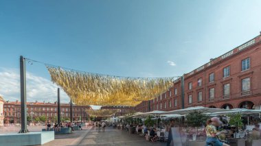 Capitole de Toulouse zaman çizelgesini gösteren panorama, Fransa 'nın Toulouse şehrinin tarihi belediye binasını ve belediye merkezini gösteriyor. Capitole Meydanı' nda mavi bulutlu gökyüzü altında birçok restoran bulunuyor.