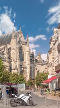Bordeaux, Fransa 'daki Basilique Saint-Michel zaman çizelgesi, yüksek kulesi olan gotik bir simgedir. İnsanlar yakındaki kafeleri seviyor, yeşil ağaçların altında ve mavi bulutlu gökyüzü, şehrin canlı cazibesini yakalıyor.
