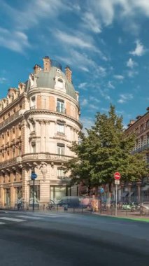 Toulouse, Occitanie, Fransa 'da Rue de Metz' in zaman çizelgesini gösteren panorama, tarihi cepheleri, dükkanları, kafeleri, trafiği ve mavi bulutlu gökyüzünü gösteriyor. Şehrin göbeğinde canlı bir şehir manzarası