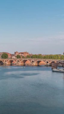 Toulouse, Fransa 'da Port de la Daurade ile Garonne Nehri ve Pont Neuf zamanapse. Bu Rönesans kemer köprüsü bulutlu mavi gökyüzünün altındaki suya yansıyor. Yeşil ağaçlı rıhtım
