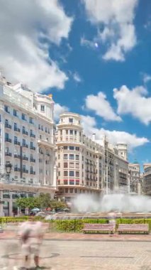 Valencia, İspanya 'da Belediye Meydanı Plaza del Ayuntamiento zaman atlaması hipervane. Büyük mimari, çiçek açan yeşillik ve bulutlu bir gökyüzünün altında su jetleri. İnsanlar canlı meydanda geziniyor..