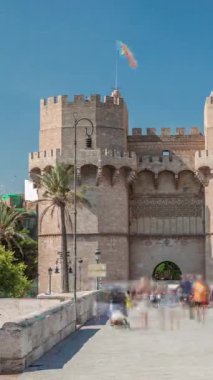 Serrans Kuleleri Torres de Serranos zaman atlaması. Valencia, İspanya 'da. Şehrin antik duvarlarından gelen büyük bir ortaçağ kapısı. Mavi gökyüzü altındaki hareketli sokak manzaraları bu tarihi yeri çerçeveler.