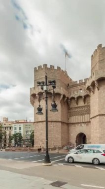 Serrans Kuleleri Torres de Serranos zaman atlaması. Valencia, İspanya 'da. Şehrin antik duvarlarından gelen büyük bir ortaçağ kapısı. Bulutlu bir gökyüzü altında hareketli bir sokak manzarası bu tarihi yeri çerçeveler.