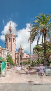 Valencia, İspanya 'da Plaza de la Reina' nın panoramik zaman atlaması. Tarihi bir kilise kulesi, hareketli kafeler ve sıcak Akdeniz semaları altında palmiyeleri olan merkezi bir çeşme..