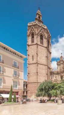 Valencia, İspanya 'da Plaza de la Reina' nın panoramik zaman atlaması. Tarihi bir kilise kulesi, hareketli kafeler ve sıcak Akdeniz mavi bulutlu gökyüzünün altında merkezi bir çeşme ile dolu canlı bir meydan..
