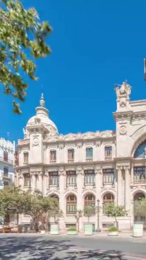 Panorama, Valensiya 'daki tarihi Postane Palau de les Comunicacions' ı gösteriyor. Şehir Meydanı Plaza del Ayuntamiento 'da. Süslü cephe, trafik ve İspanya şehir merkezinde mavi bir gökyüzü..