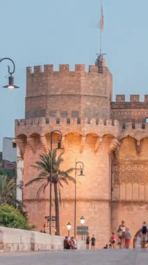 Serrans Kuleleri Torres de Serranos günden geceye Valencia, İspanya 'daki geçiş zamanı. Şehrin antik duvarlarından gelen büyük bir ortaçağ kapısı. İnsanlar tarihi bir dönüm noktasının yakınındaki bir köprüde yürüyorlar.