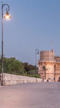 Serrans Kuleleri Torres de Serranos günden geceye Valencia, İspanya 'daki geçiş zamanı. Şehrin antik duvarlarından gelen büyük bir ortaçağ kapısı. İnsanlar tarihi bir yere yakın bir köprüde yürüyorlar.